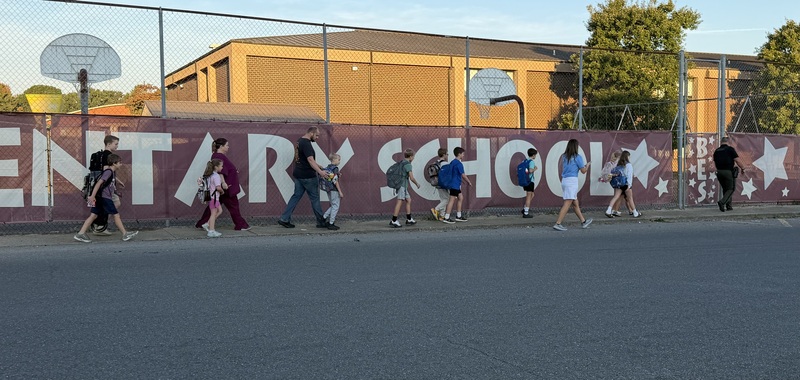 Students walking on sidewalk while approaching school playground on International Walk to School Day