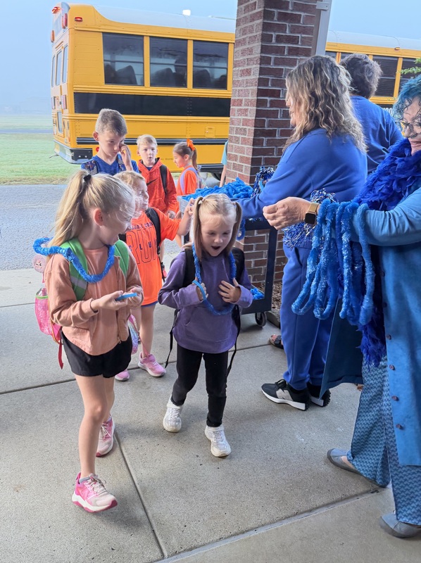 SMES students getting off bus and being give blue bands and leis