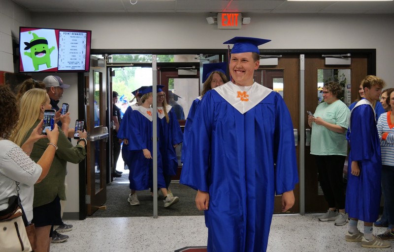 Senior walking into BES in cap and gown