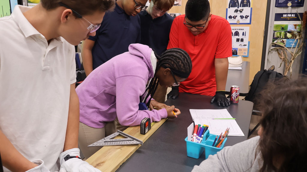 A student using a tape measure as other students observe.