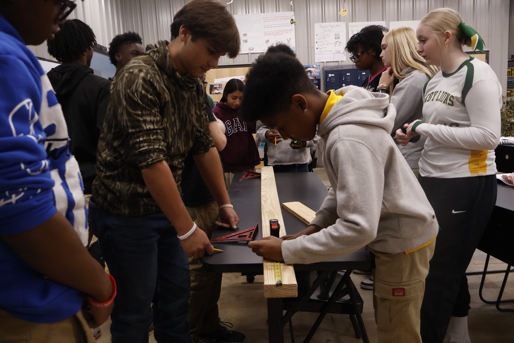 A student using a tape measure as other students observe.