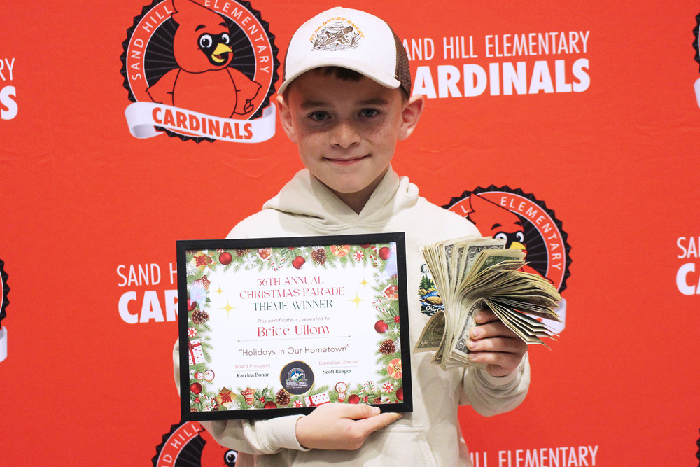 Brice poses with his certificate and the 100, one-dollar bills he won for naming the 2026 Marshall County Chamber of Commerce Christmas Parade.