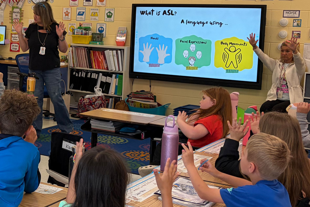 Classroom scene with students gathered around an interactive display.