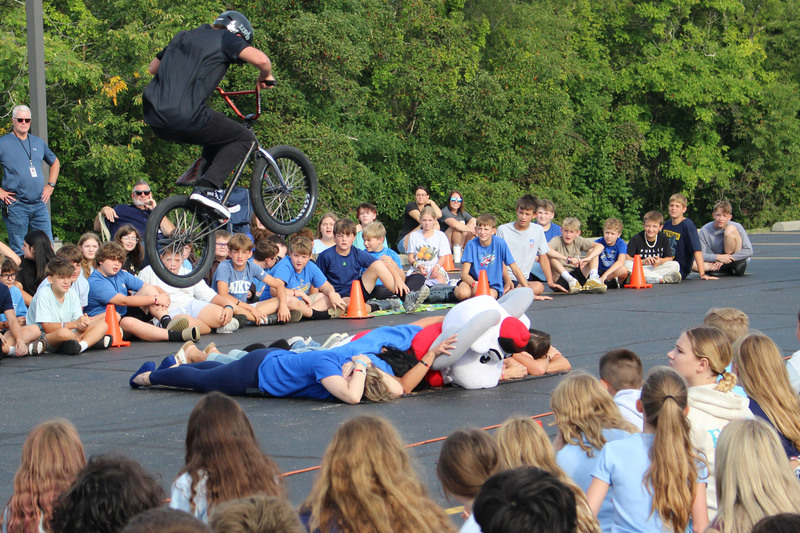 A group of people watching a performer on a BMX bike doing stunts in an outdoor setting.