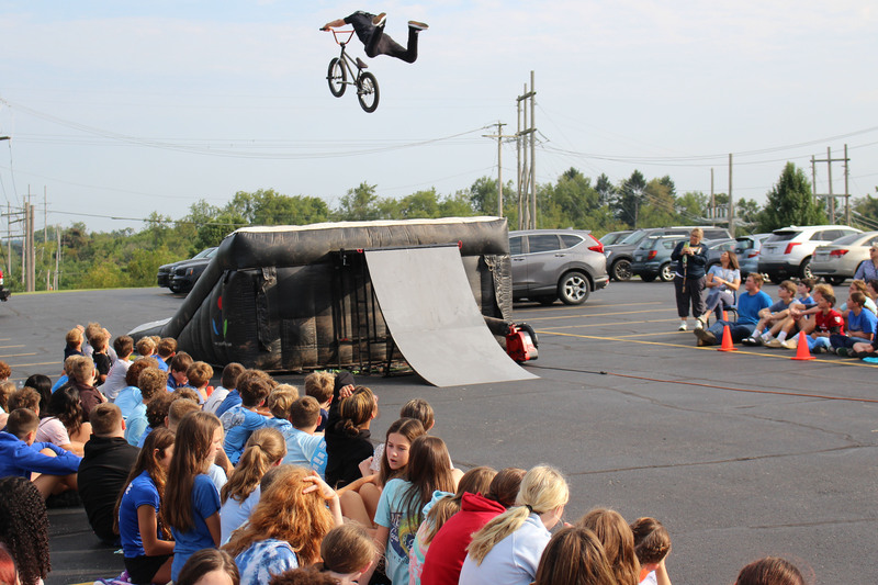 A BMX rider performing a trick over a crowd of spectators watching an outdoor event.