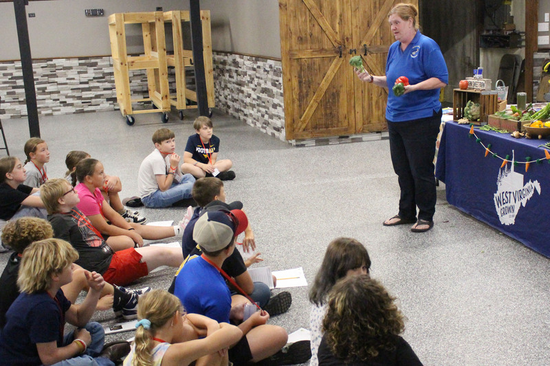 A group of people sitting on the floor listening to a man standing and speaking to them in what appears to be a community center or classroom setting.