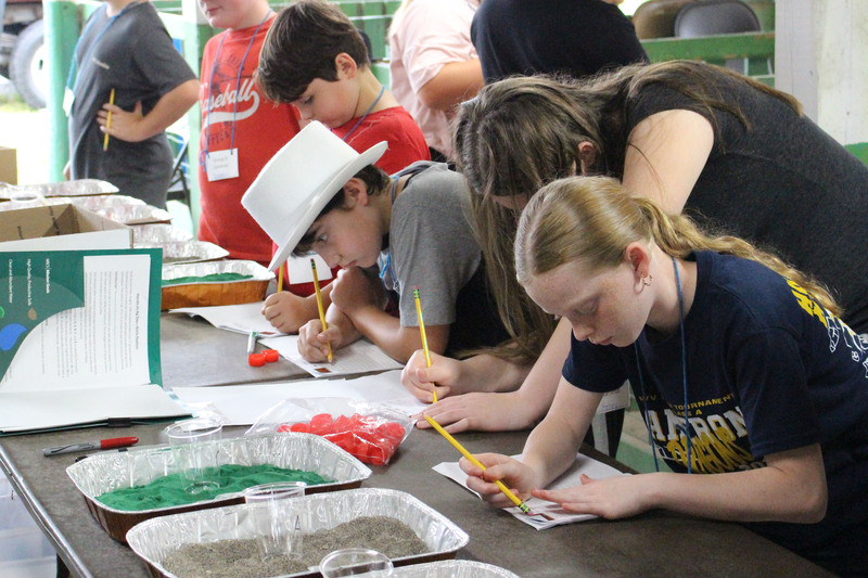 A group of students working together at a table, each engaged in an activity involving tools and materials.