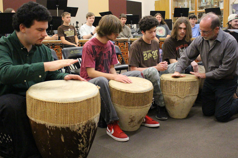 Group of people sitting in a circle playing djembe drums during a workshop or class in an indoor community space.