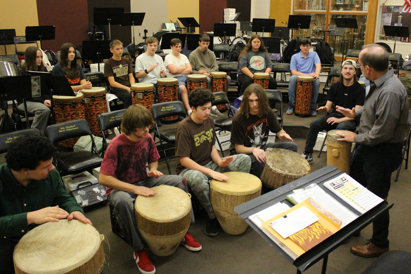Group of people sitting in a circle playing djembe drums during a workshop or class in an indoor community space.