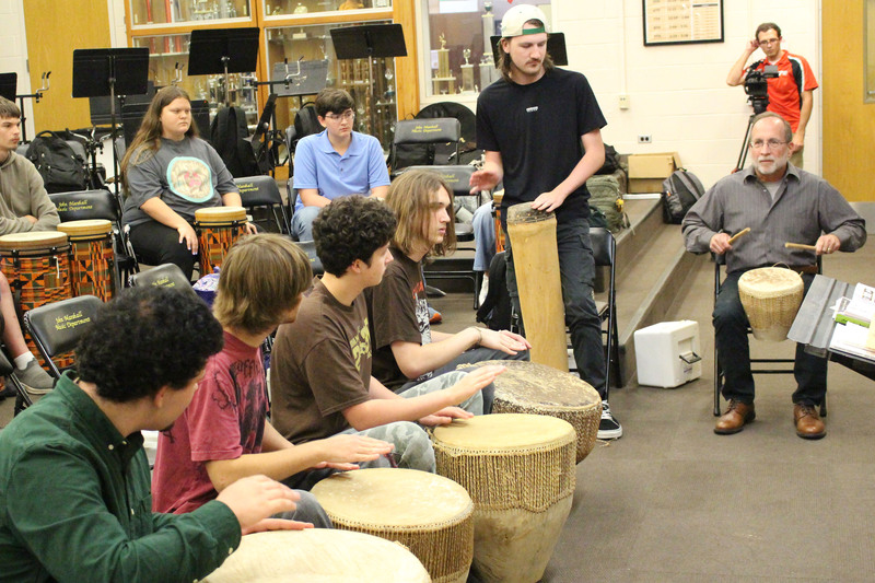 Group of people sitting in a circle playing djembe drums during a workshop or class in an indoor community space.