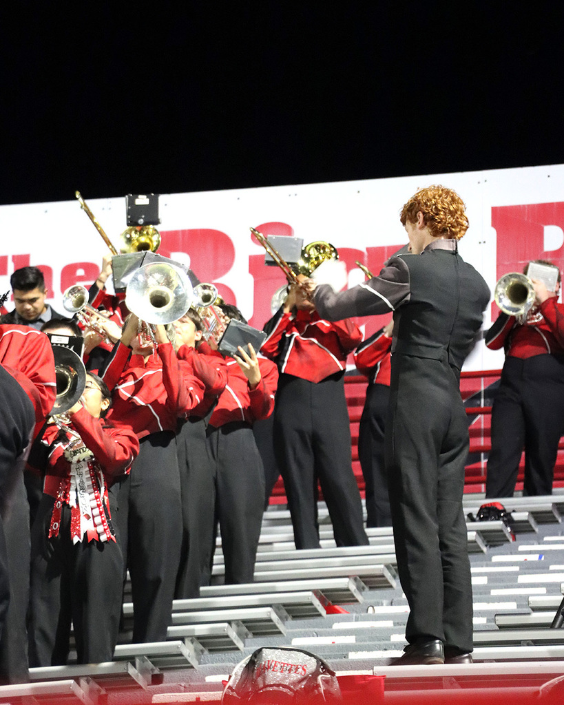 Band members playing instruments in red and black uniforms in the bleachers.
