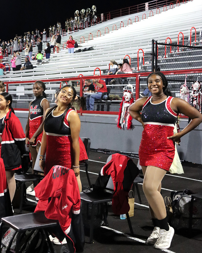 Students in red and black uniforms standing near black chairs posing for a photo. 