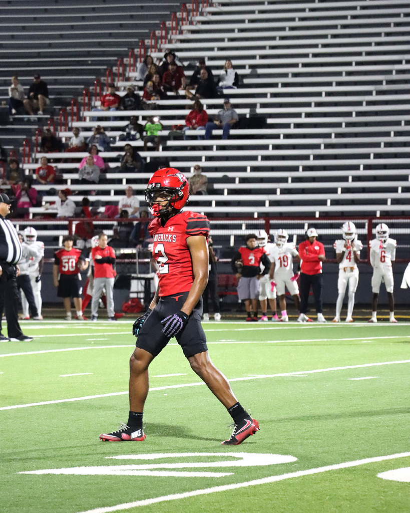 A football player getting ready for the next play on a field with other players in red jerseys standing on the sidelines.