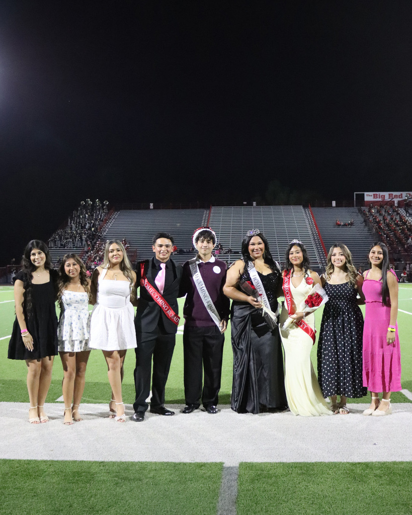 Nine students on field, some wearing sashes, with stadium bleachers in background and stadium lights on.