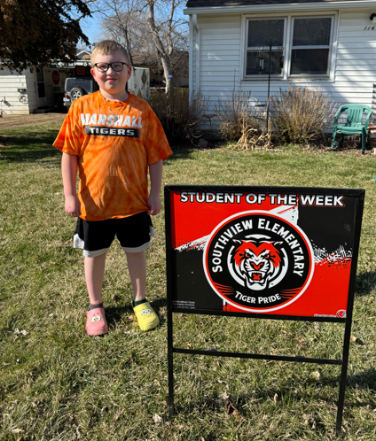 young man standing next to a sign that says student of the week.
