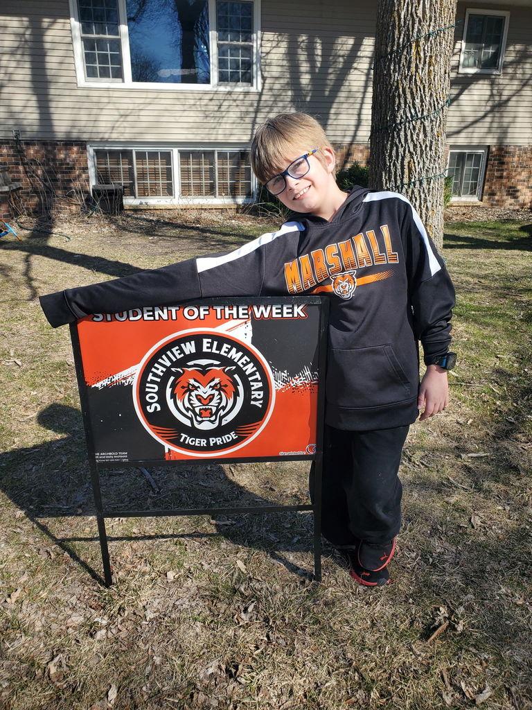 young man standing next to a sign that says "student of the week"