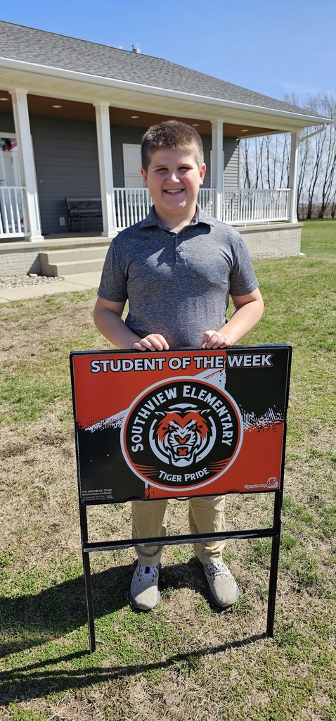 young man standing behind a sign that says "student of the week"
