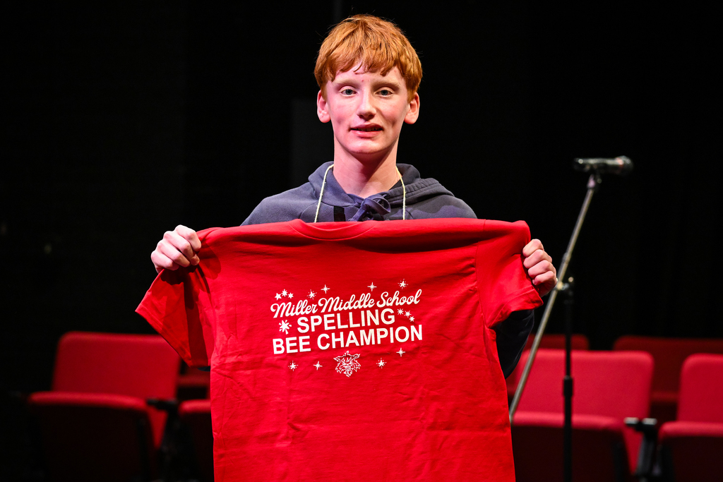Student Tyler Beare holding his spelling bee champion shirt
