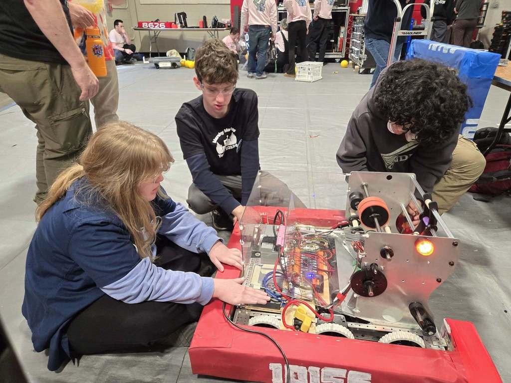 Three robotics team working on robot