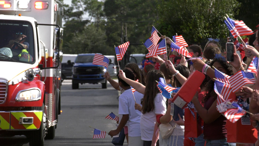 Students at Hidden Oaks Middle School line up in the school's bus loop to greet and handout the Hero Bags made for local first responders as they waive flags