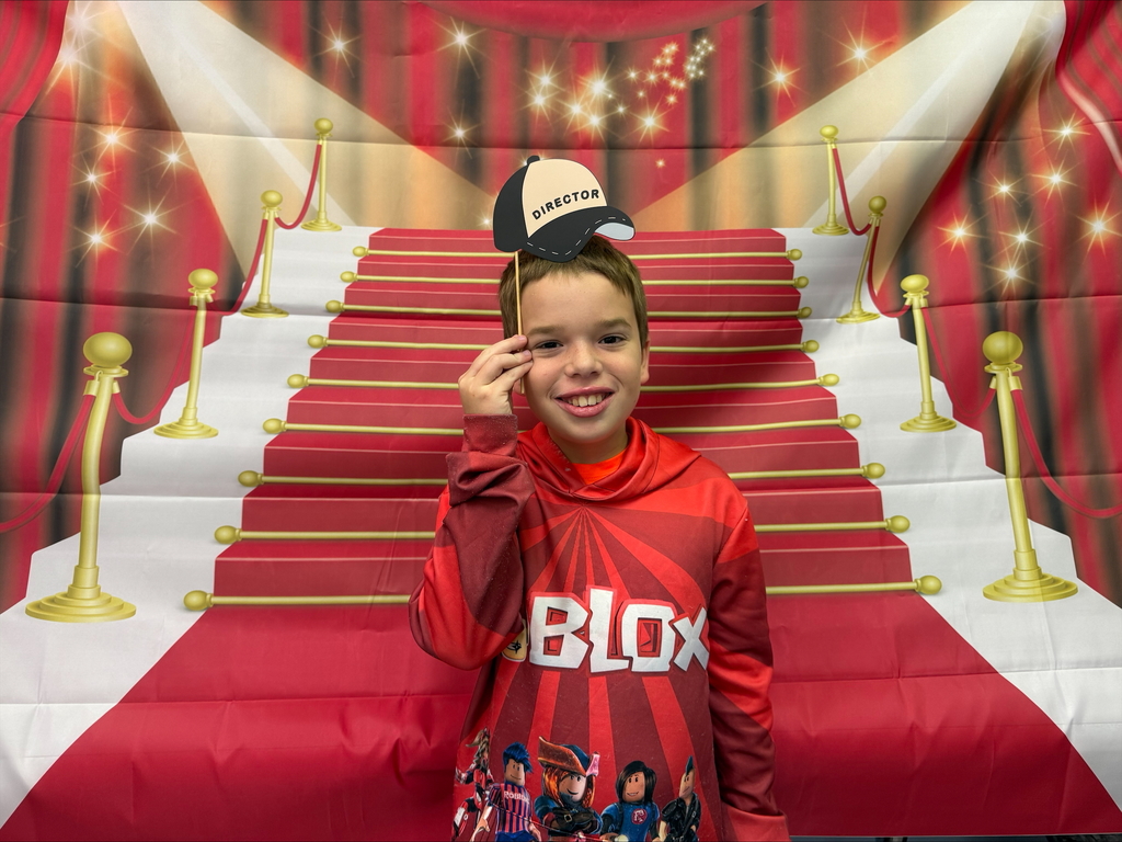 A student poses with a Director hat in front of a red carpet.