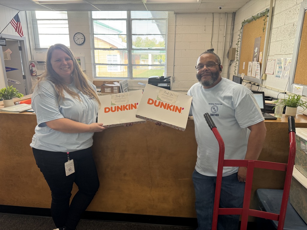 E.J. Hayes Elementary staff members Mrs. Thompson and Mr. Roberson smile while holding two boxes of Dunkin’ Donuts provided by H&R Block of Williamston to welcome staff on the first Required Work Day of the school year.