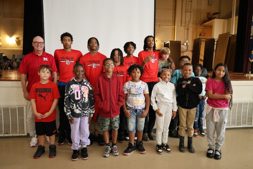 Coach Gary Hall poses in the AHES auditorium with some MHS basketball players and AHES students