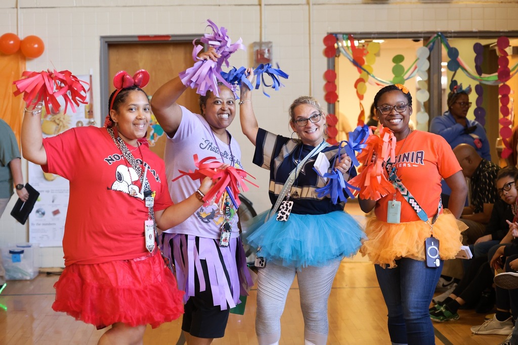 AHES teachers in colorful outfits hold paper pom poms and smile brightly