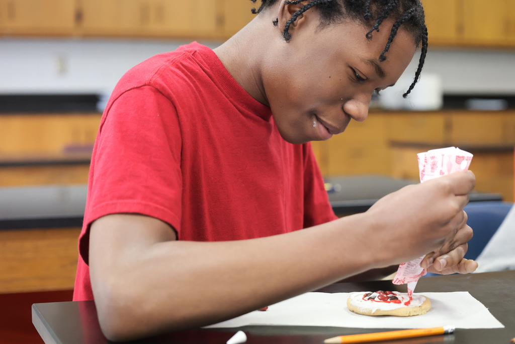 An eighth grade student carefully adds red icing to his cookie while constructing an edible model of a lithium atom during science class.