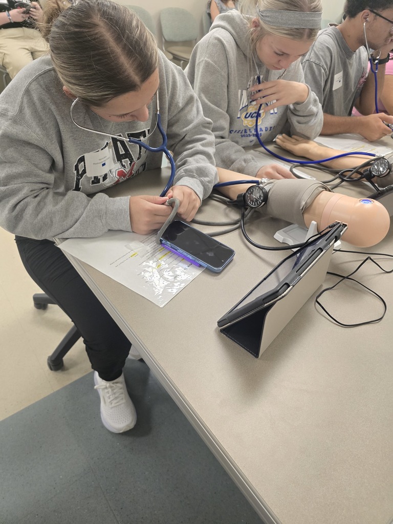 Hanna Bass with a stethoscope and collecting a blood pressure on a practice device.