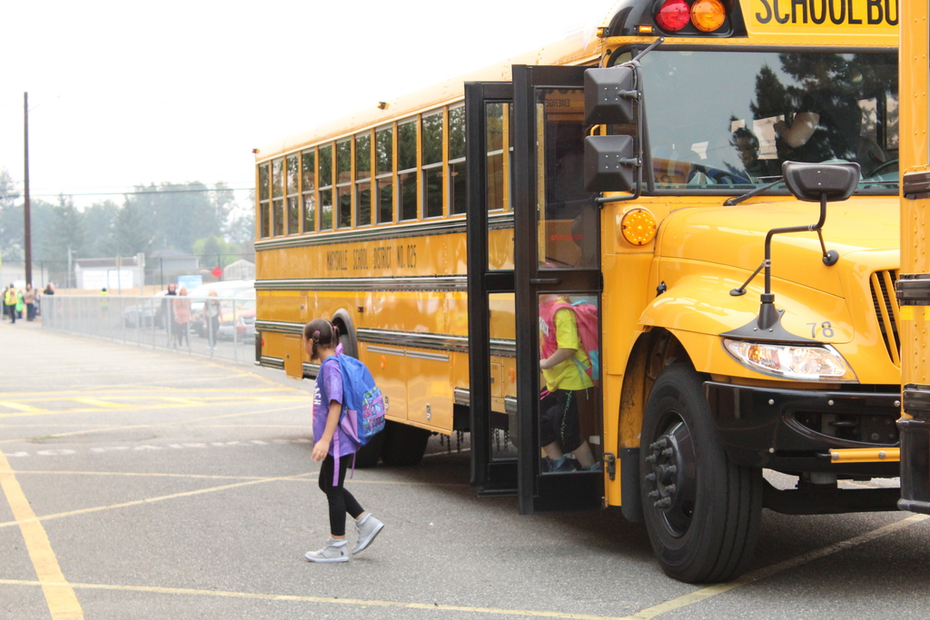 A Marysville School District is seen on the right side of the frame. A child in a purple shirt is walking away from the school bus. 