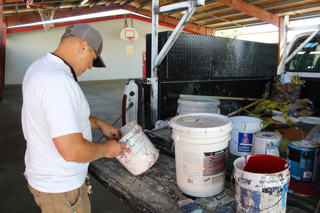 A man stands in front of buckets full of paint that are sitting in the back of a truck under