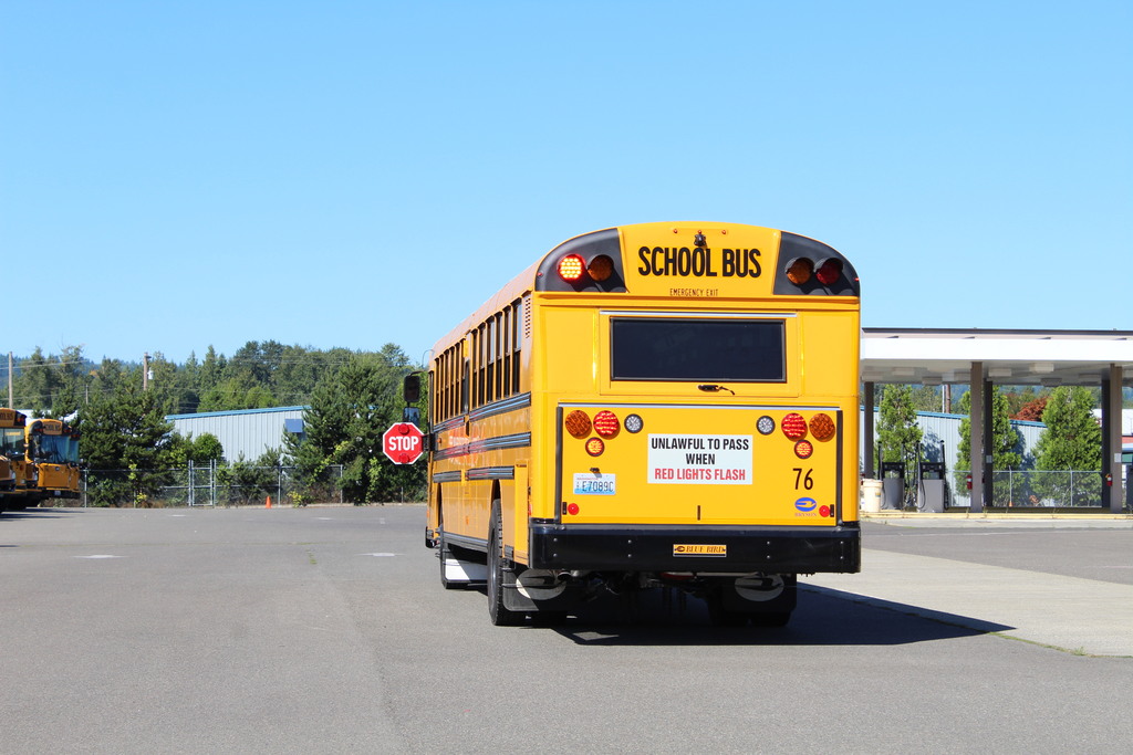 a yellow school bus is stopped with red lights on, and a stop arm extended