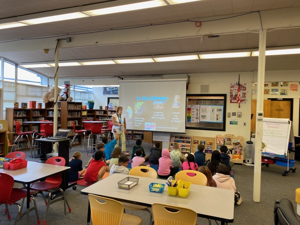 children are sitting in a library listening to the librarian speak