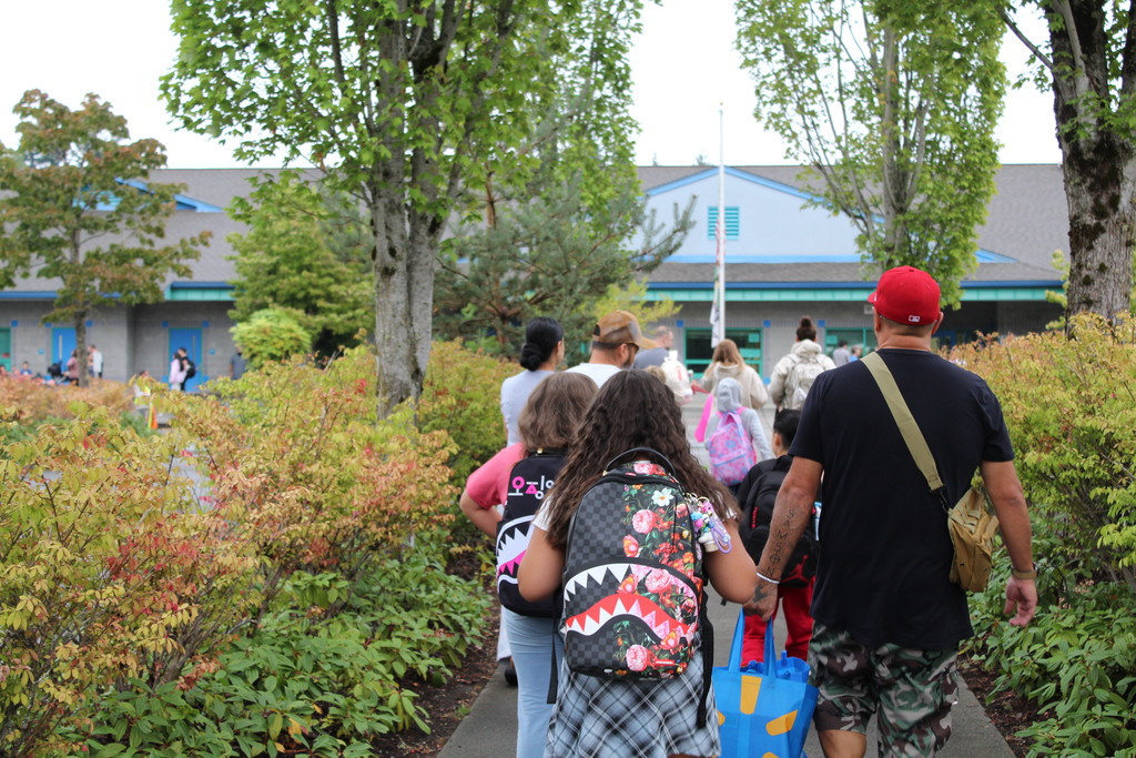 a group of people walk toward a blue building with shrubs alongside them