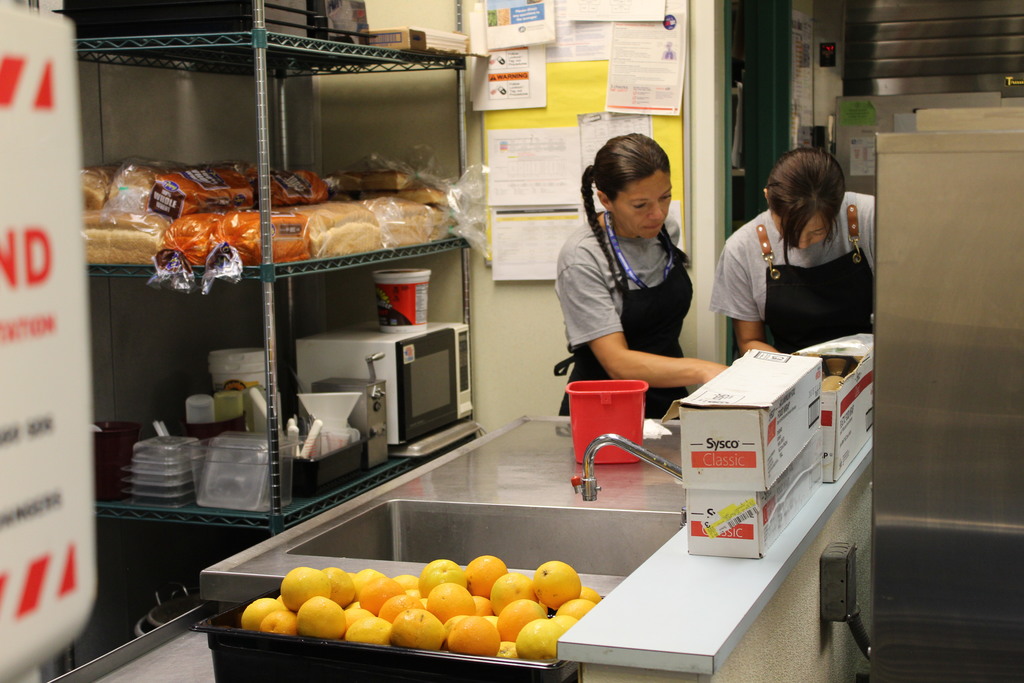 two people look down in a school kitchen with oranges nearby