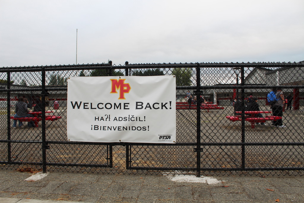 A welcome sign is on a fence with students behind 