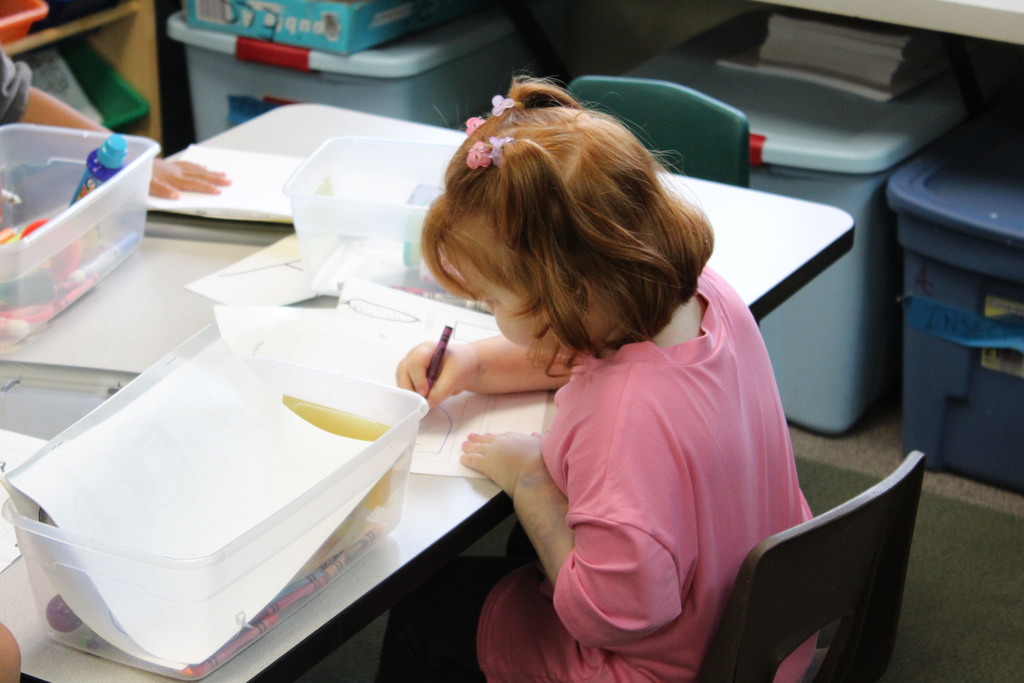 A student with red hair and a pink shirt is drawing 