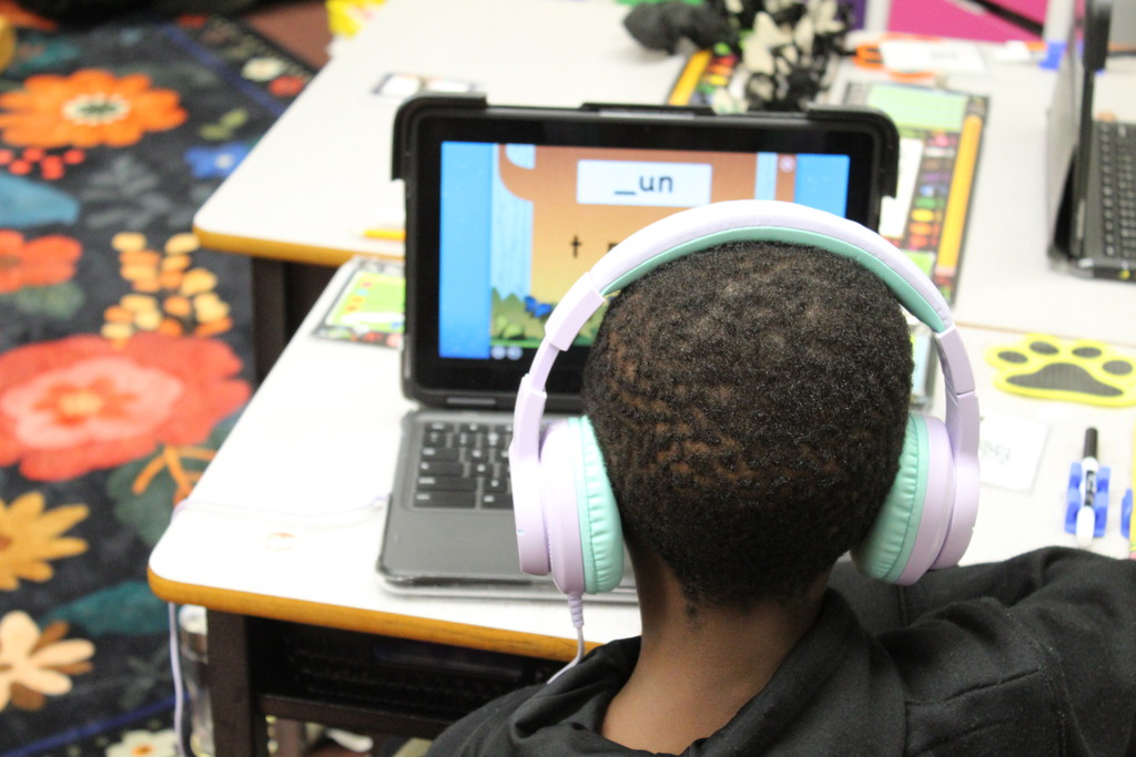 A student with headphones on looks at a device to do a literacy assignment