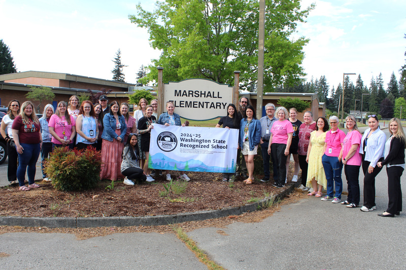 Staff from Marshall Elementary hold up a sign in front of the Marshall Elementary sign, and they are smiling!
