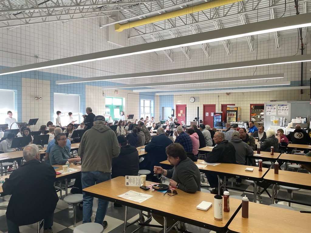 A photo of the Veteran's Day Breakfast event in the Boynton cafeteria. The school band is getting ready for their performance while people enjoy their food at the tables.