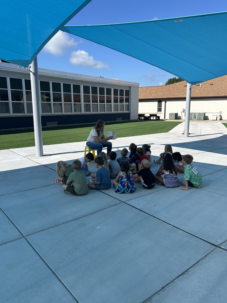 A kindergarten teacher takes her students outside to enjoy the weather and read a good book.
