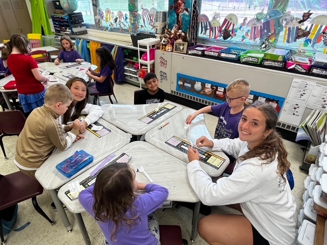 Mascoutah high school student helping students at a table glue yarn to a spoon.