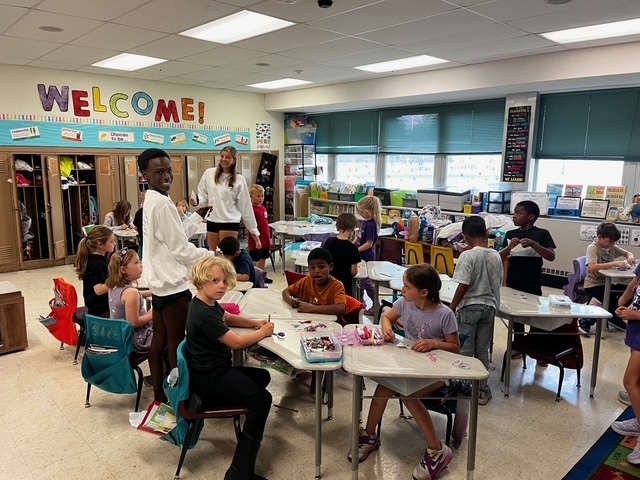 Picture is of high school students reading to kids at the elementary and helping them make a craft.