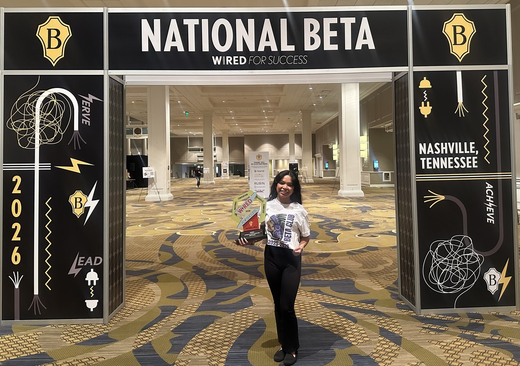 Olivia Lubang holding her trophy under the National Beta Convention entrance!