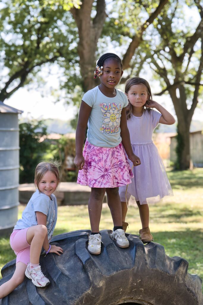 Three girls standing on a tractor tire.