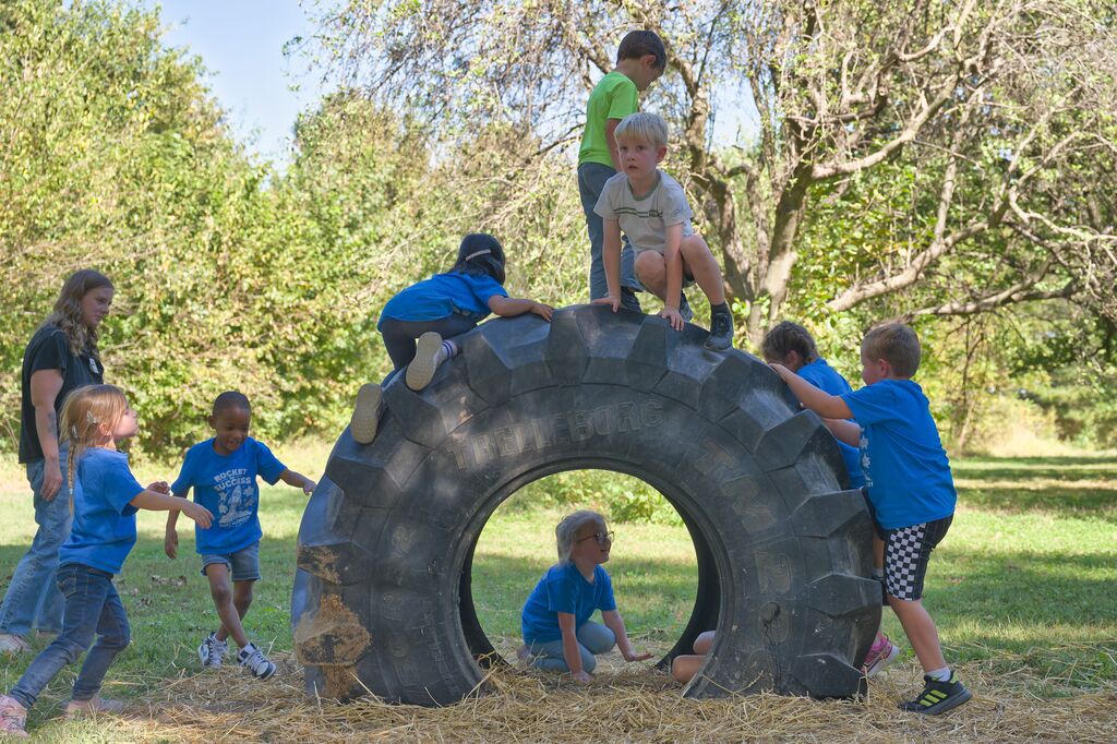 Kindergarteners playing on and under a tractor tire.