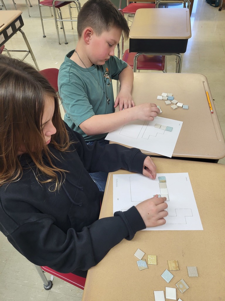 Students in a 3rd grade classroom working on math activities involving area and perimeter, using shapes and hands-on materials.