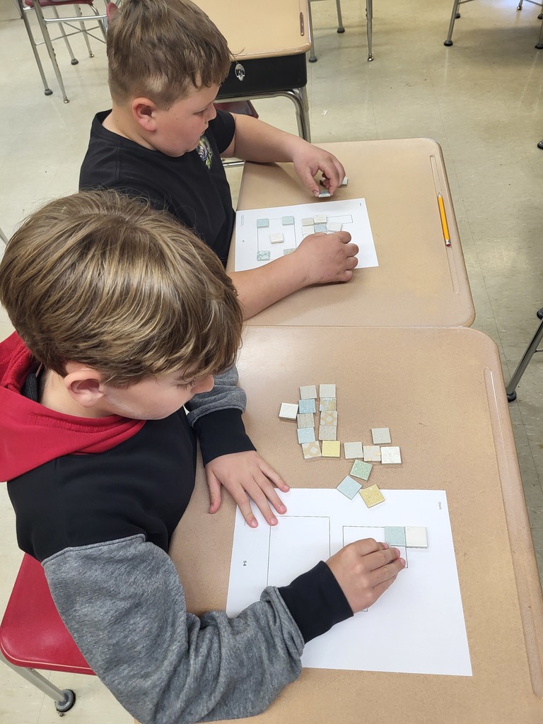 Students in a 3rd grade classroom working on math activities involving area and perimeter, using shapes and hands-on materials.