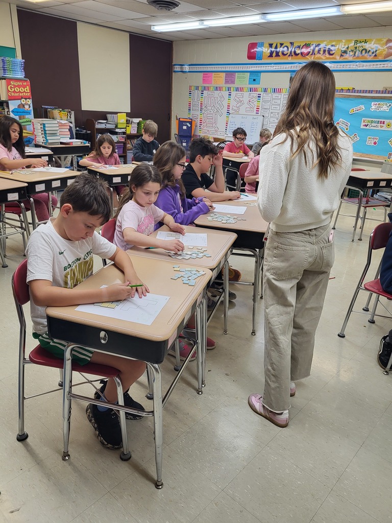 Students in a 3rd grade classroom working on math activities involving area and perimeter, using shapes and hands-on materials.